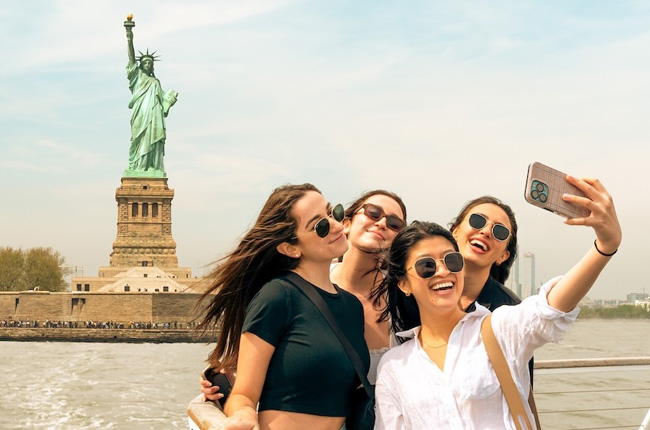 Friends taking a selfie in front of the Statue of Liberty